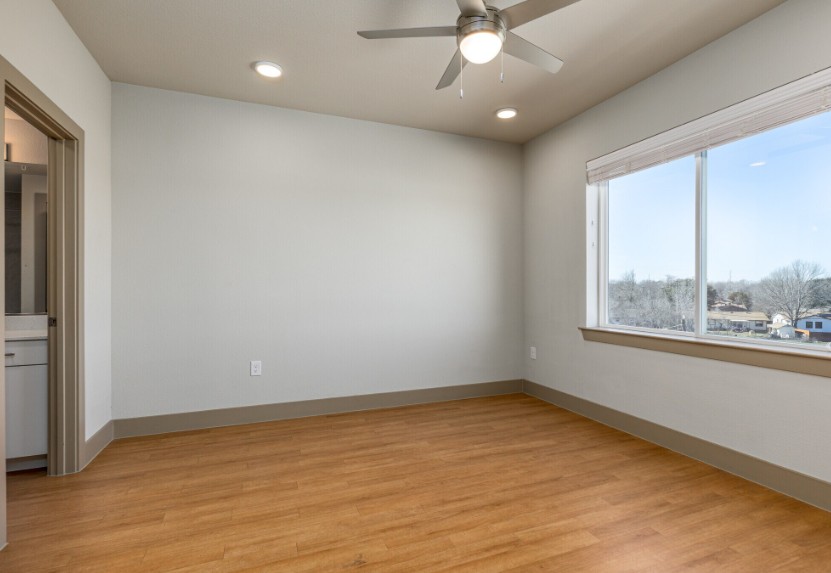 A room with a ceiling fan and a window overlooking a residential area.